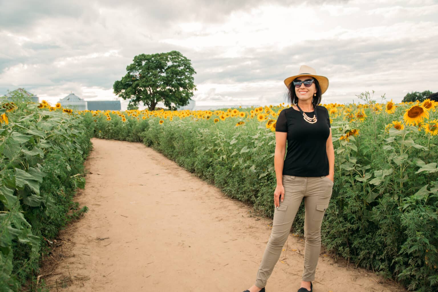 Lindsey wearing a straw fedora and Anatomie clothing while standing in a sunflower field