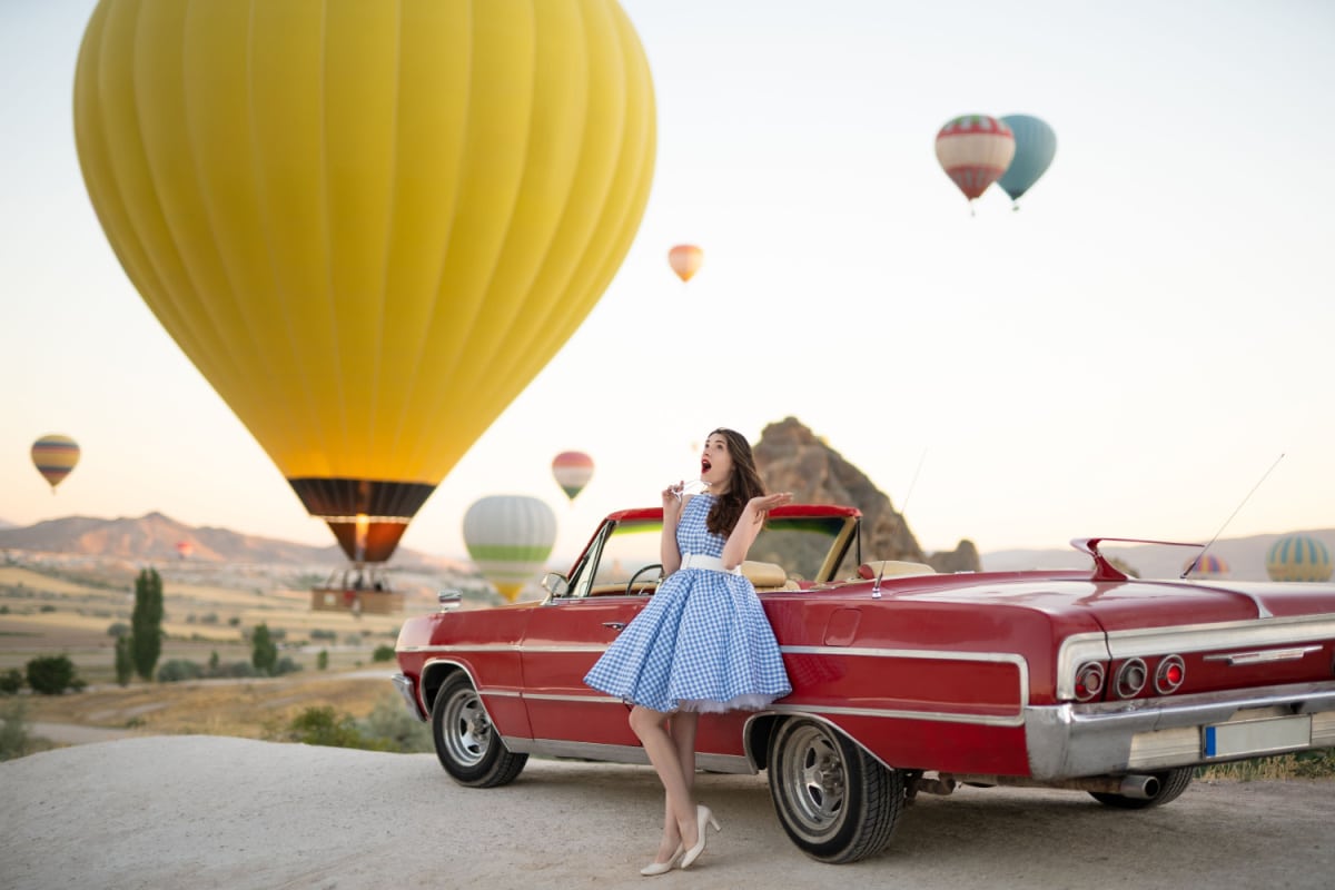 beautiful girl in retro style posing near a vintage red cabriolet car on background of balloons in Cappadocia