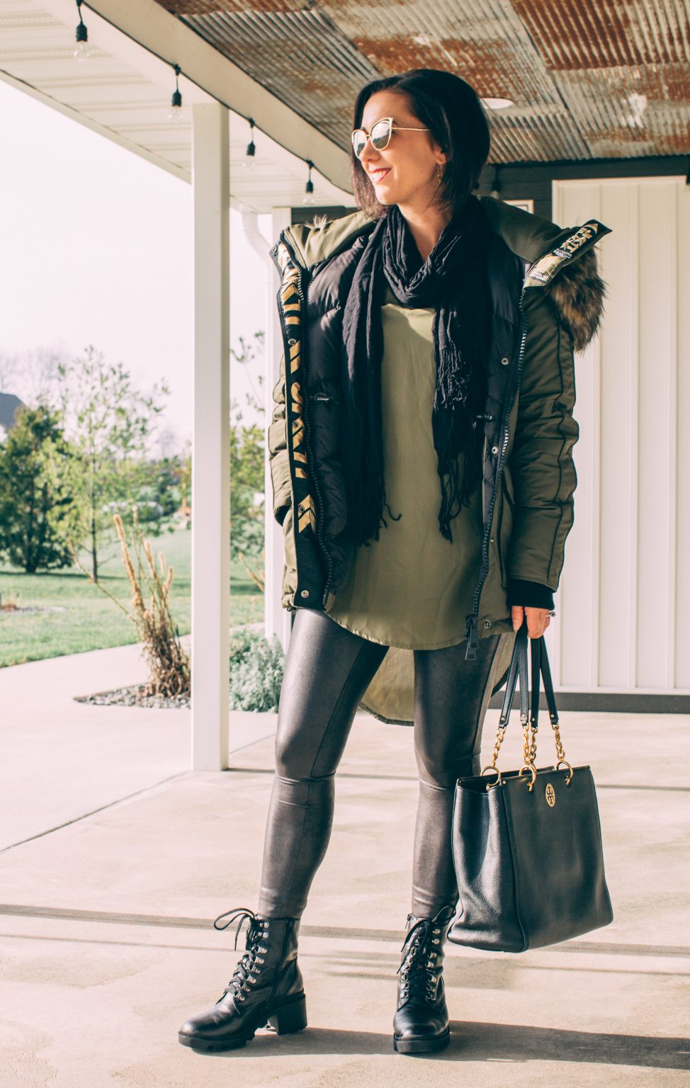 a woman wearing a green winter coat with a green tunic, faux leather leggings, black combat boots and carrying a large black leather tote