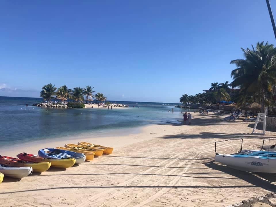 A view of the beach near the Holiday Inn in Jamaica. Kayaks are lined up on the shoreline, and resort guests swim in the ocean in the distance.