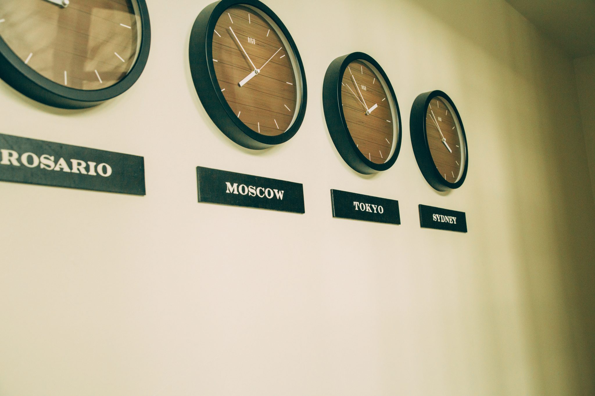 A closer look at the time zone wall created with wall-mounted analog clocks set to different locations. Each clock as a placard underneath indicating the time zone.
