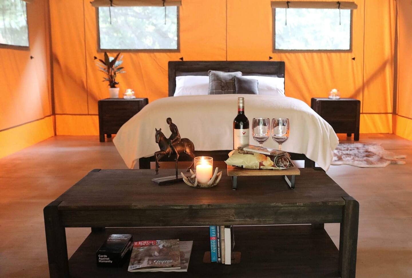 Inside a luxury glamping tent featuring a bed, nightstands, and table with wine and burning candle on it