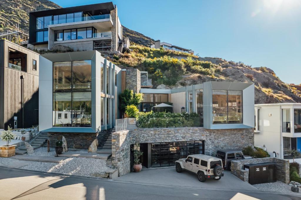 Modern Airbnb in New Zealand with glass exterior, built into a cliff with jeeps parked in the driveway 
