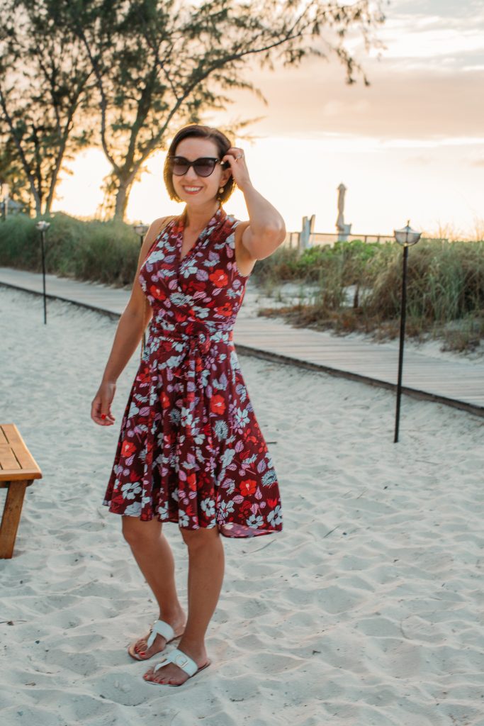 Lindsey wearing a red and white floral wrap dress from Karina Dresses, standing on the sand