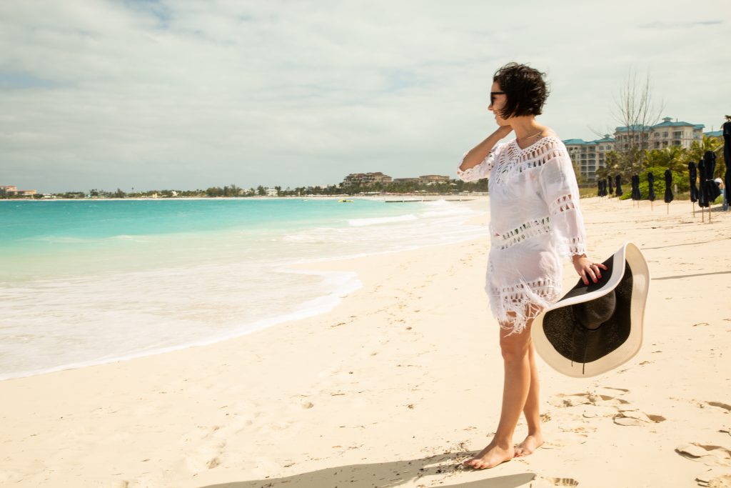 A women wearing swimwear and cover up while holding a hat in her hand on Turks and Caicos Islands.