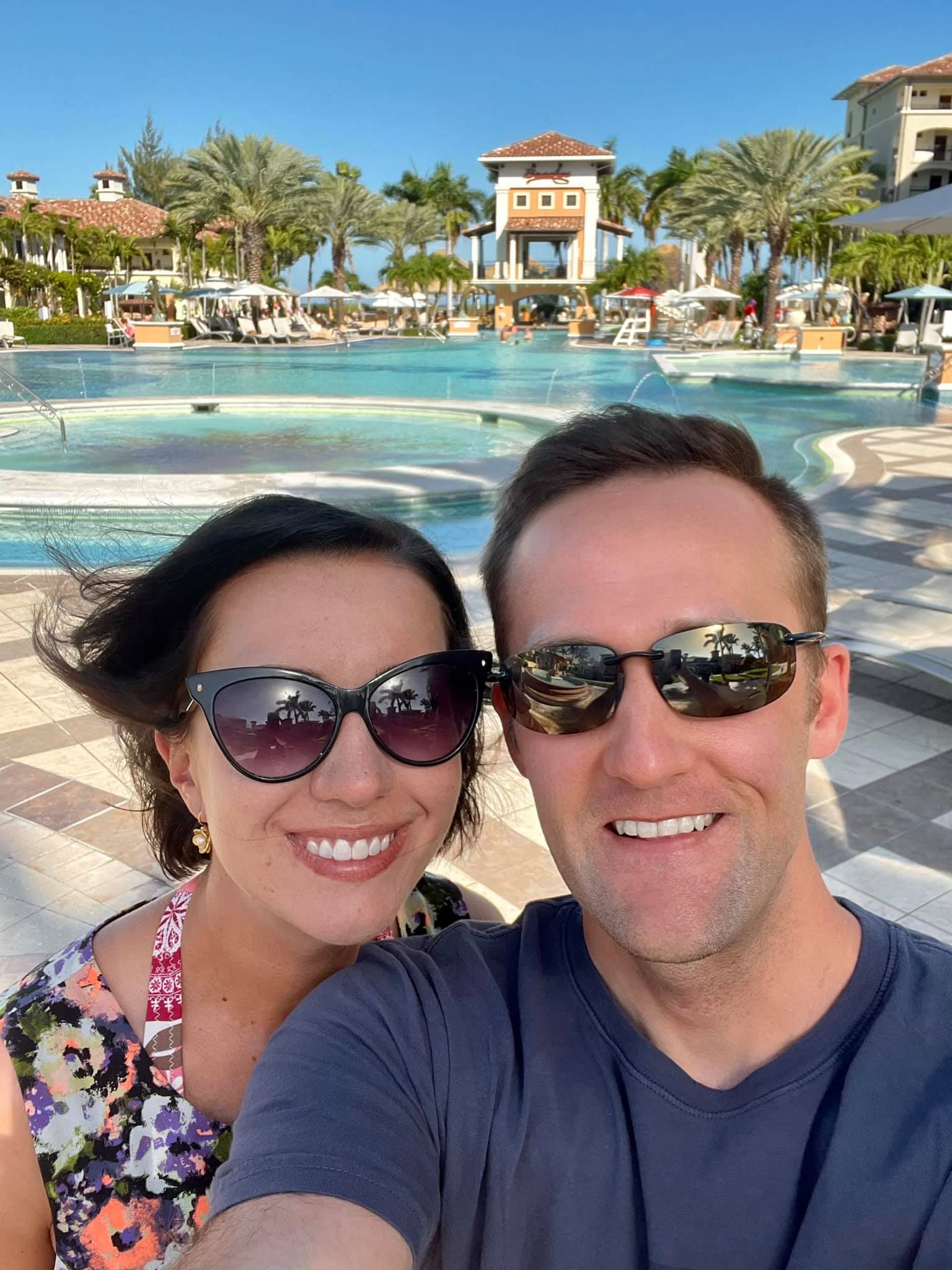 Lindsey and Zac taking a selfie in front of a pool at a tropical resort in Turks and Caicos