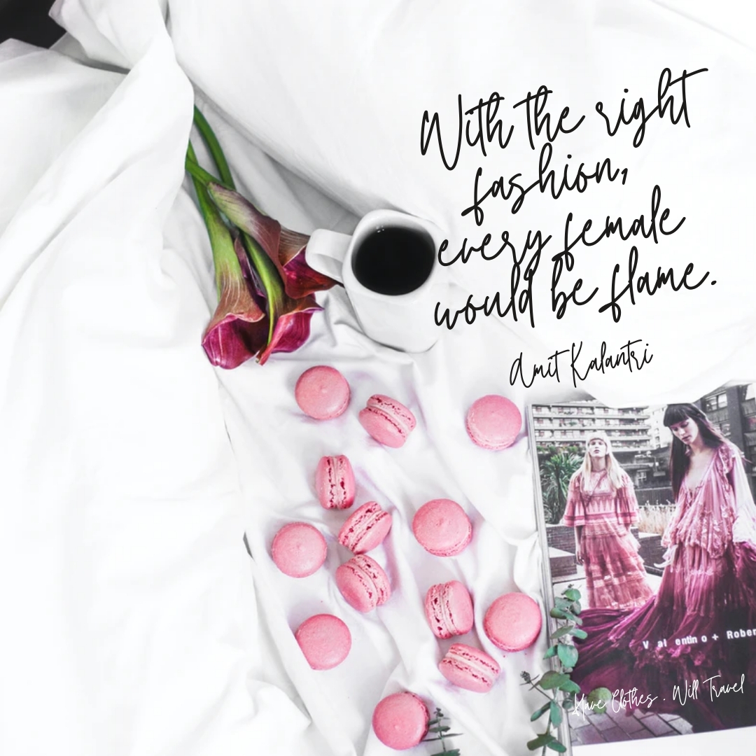 An overhead photo of pink flowers, pink macarons, a mug of black coffee, and a fashion magazine laid out on a white linen bed. Black cursive text on the image reads, "With right fashion, every female would be a flame. ― Amit Kalantri, Wealth of Words"