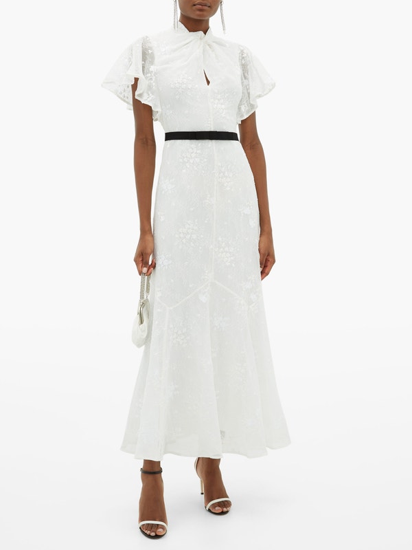 A model wears a modest lace wedding down. The maxi style dress has short cap sleeves and a high neckline. A thin black belt wraps around the waist.