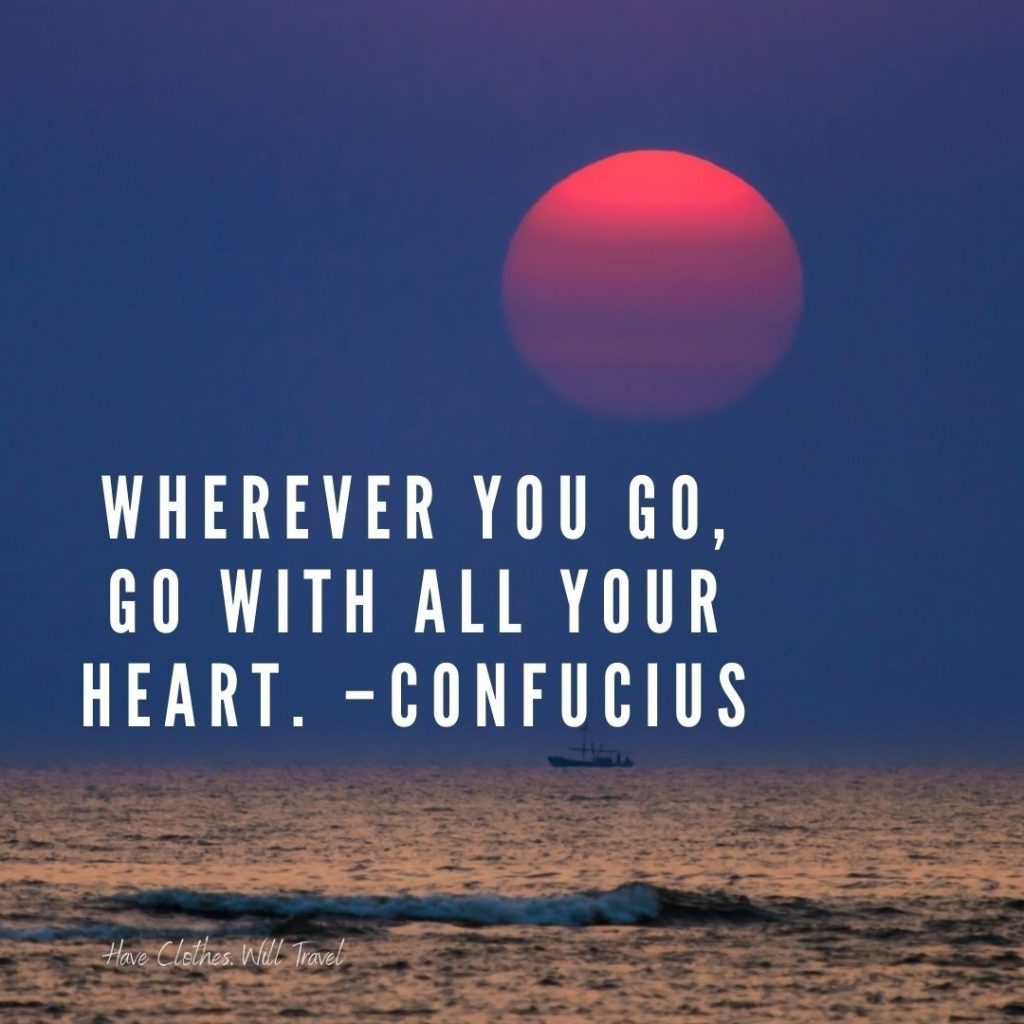 A red sun sets over the horizon of the sea, with a silhouette of a boat in the distance. Text on the image reads, "Wherever you go, go with all your heart. - Confucius"