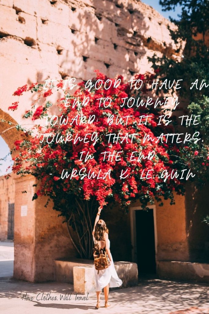 A woman stands under a large tree, reaching up and admiring the red flowers on the branches. White text across the image reads, 