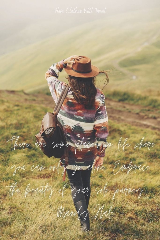A woman walks down a grassy hillside. White text across the image reads, "There are some places in life where you can only go alone. Embrace the beauty of your solo journey. - Mandy Nale"