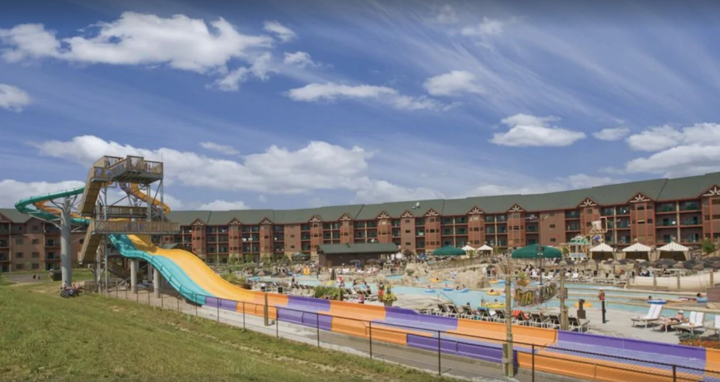 An exterior shot of the large waterpark at Wyndham Glacier Canyon, a Wisconsin Dells resort that features four stories of condo vacation rentals, multiple outdoor pools, splash pads, and water slides.
