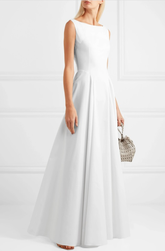 A model wears a simple, elegant, modest wedding dress made from cotton gabardine fabric. The bodice of the dress is fitted with a high neckline, but extends down into a flared floor-length skirt.