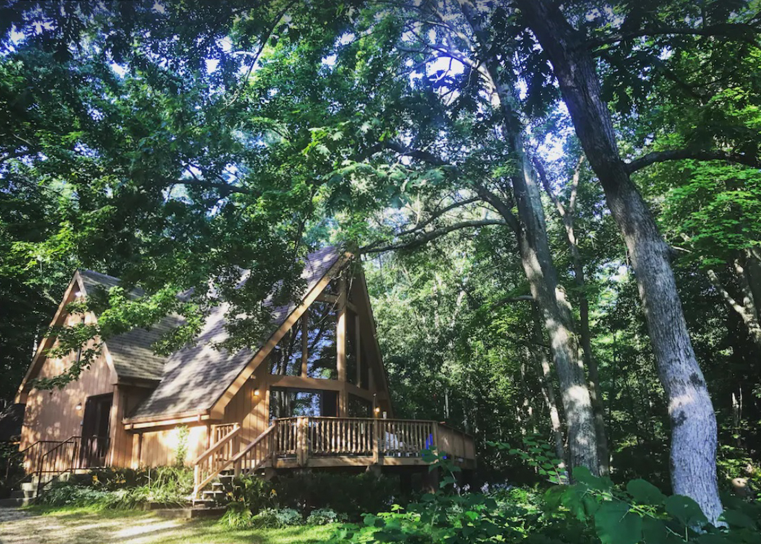 A quaint a-frame cabin nestled in the woods in the Wisconsin Dells. The cabin features a large floor-to-ceiling wall of windows that overlook a large private deck.