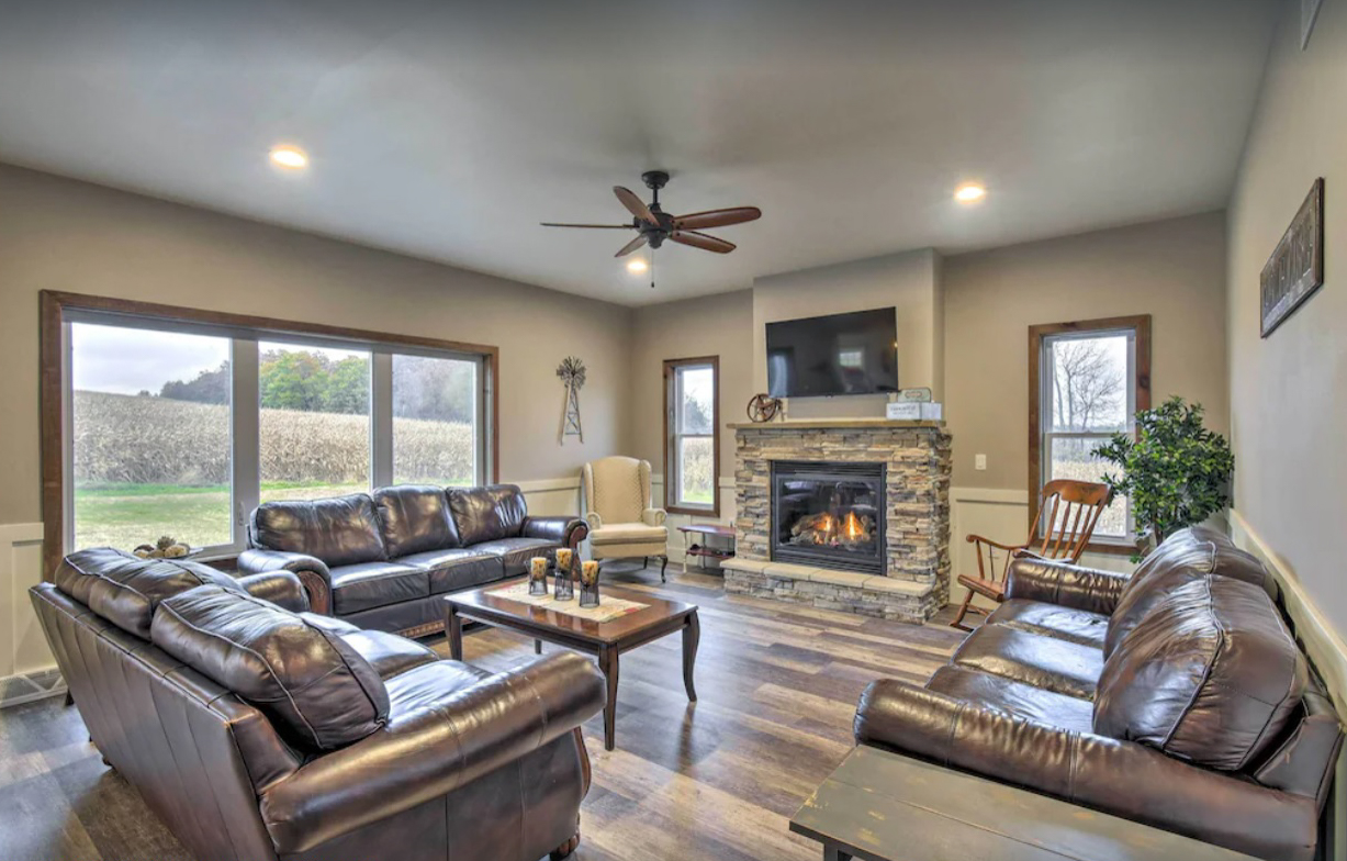 A cozy modern living room with three leather couches and a coffee table facing a stone fireplace and flat screen TV.