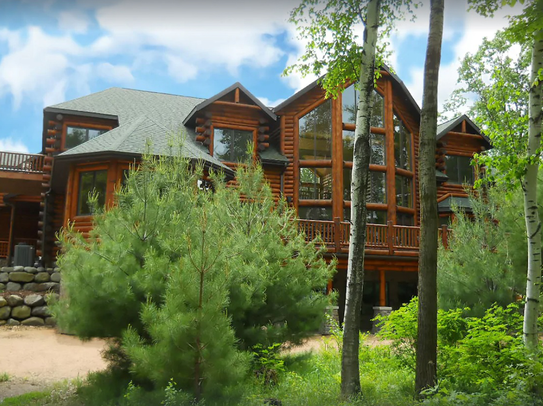 A giant log cabin mansion is nestled in the Wisconsin Dells woods. The two-story cabin has a stacked log façade and walls of windows and multiple private decks and balconies.