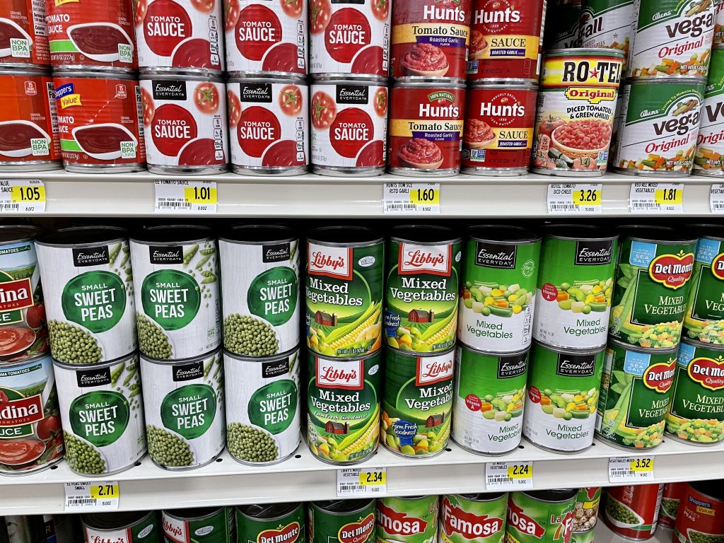 Cans of food items such as tomato sauce, mixed vegetables, and sweet peas in a grocery store in Turks and Caicos.