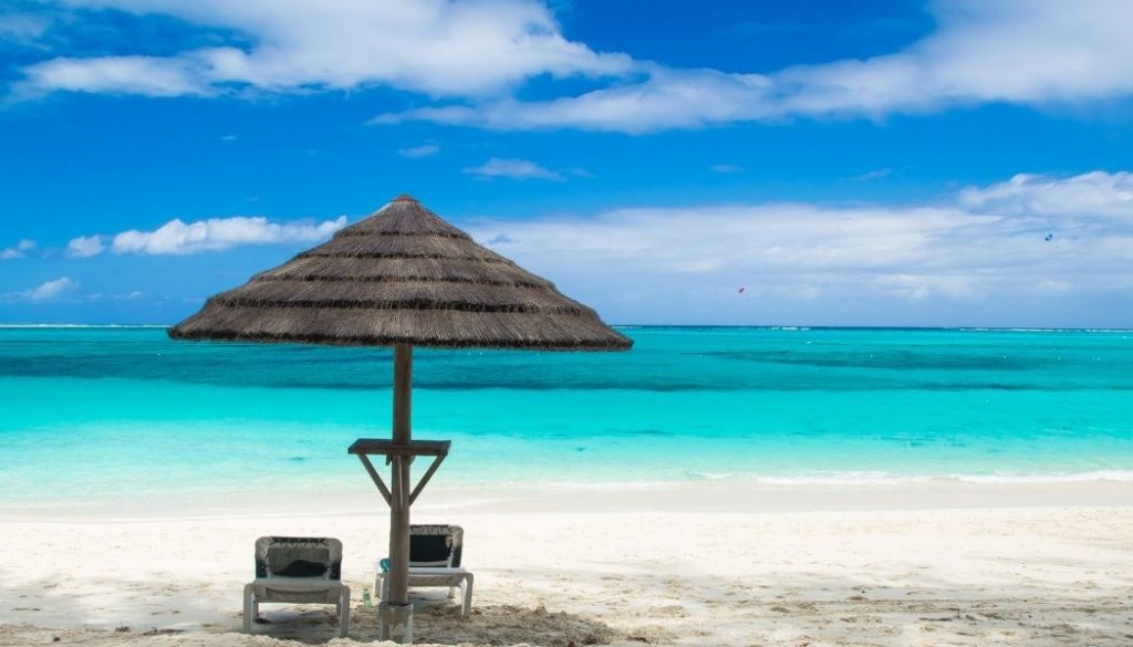 A serene blue beach with an umbrella and two chairs in Turks and Caicos.