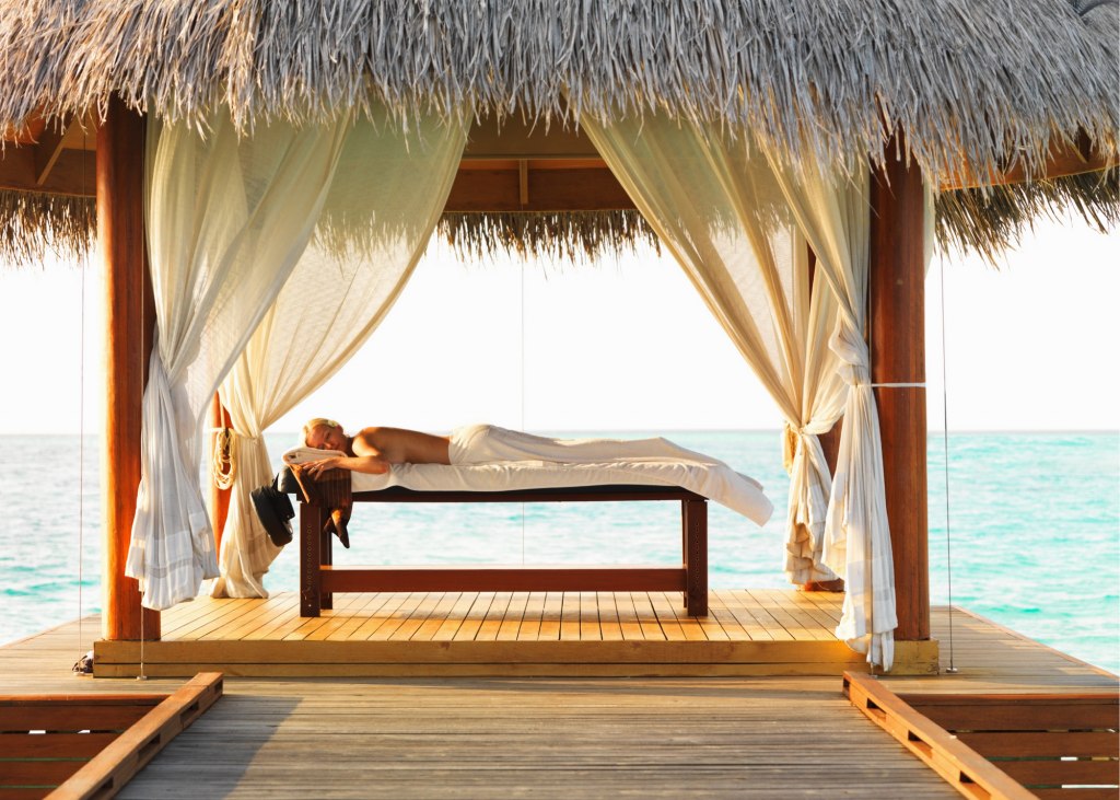 A woman is laying under a thatched gazebo on a massage table during a luxury spa treatment.