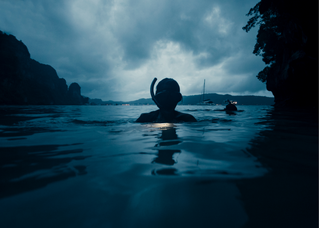 A person night snorkeling in the water under a dark sky at Smith’s Reef.