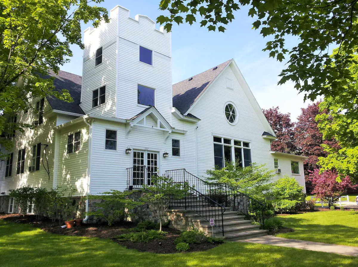 An exterior image of a church, renovated into a unique vacation rental in Door County, WI. The outside of the home has white siding and plenty of windows, with stairs leading up to the front doors.