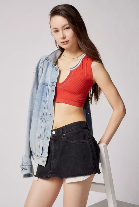Young woman with long dark hair wears Urban Outfitters Out From Under Go For Gold Seamless Top with a jean jacket and black jean shorts