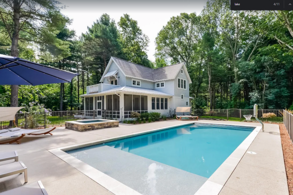 A house with a pool and chairs in the backyard - a wide angle view of a Cozy 4-bedroom Lake Trail Treehouse Cottage with Heated Pool and Hot Tub in Saugatuck.