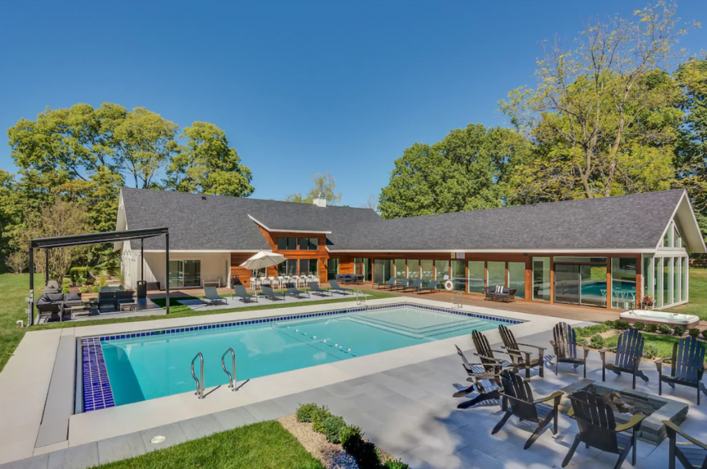 A large backyard with a pool and patio furniture - Apple Blossom 3-home Luxury Rental Estate in New Buffalo, Michigan.