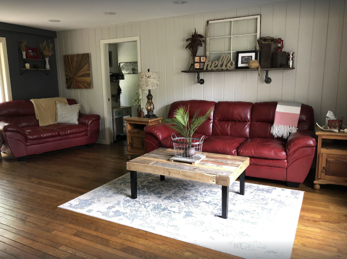 A homey living room decorated with farmhouse style decor and two red leather couches and white shiplap style walls.