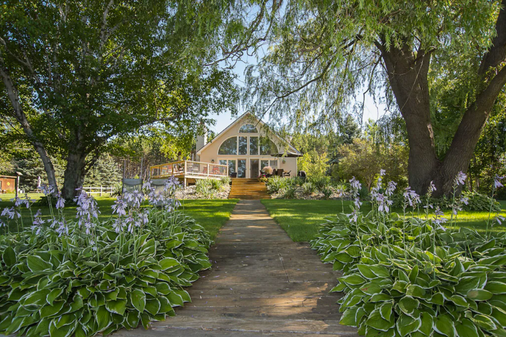 A wooden walkway leads to a house in a wooded area - a wide angle Contemporary 3-bedroom, 2-bathroom Rental Home on the Narrows of Lake Leelanau.