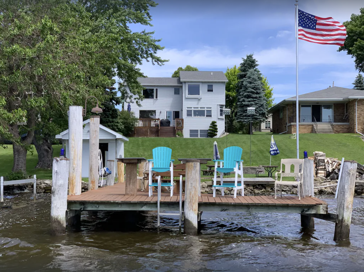 An exterior image of a two-story house in the background of the photo, with a large lawn that extends to a small pier on Lake Butte des Morts in Oshkosh WI.