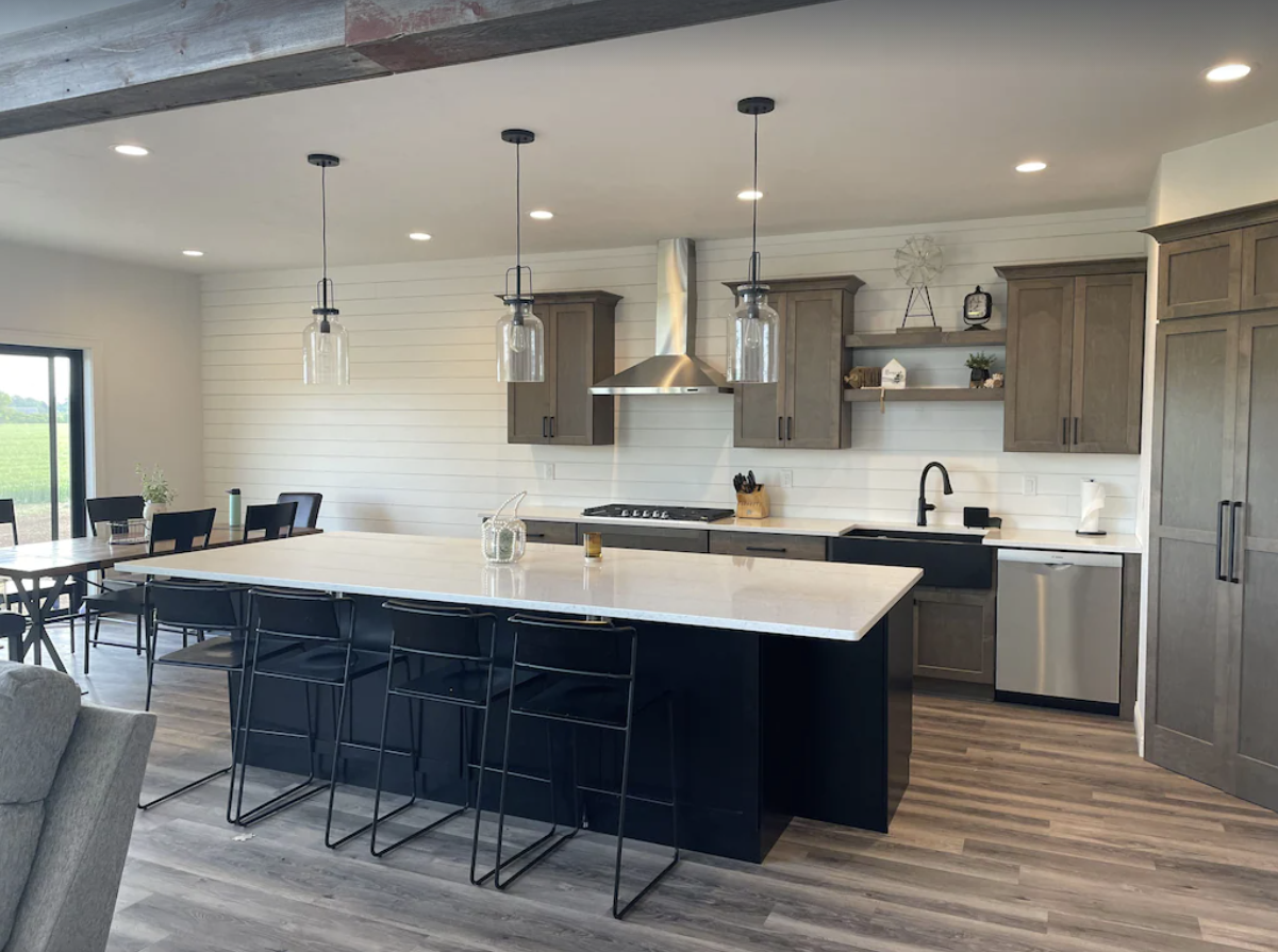 A large, modern kitchen with white subway tiled walls, brown cabinets, white countertops, and a large island breakfast bar.