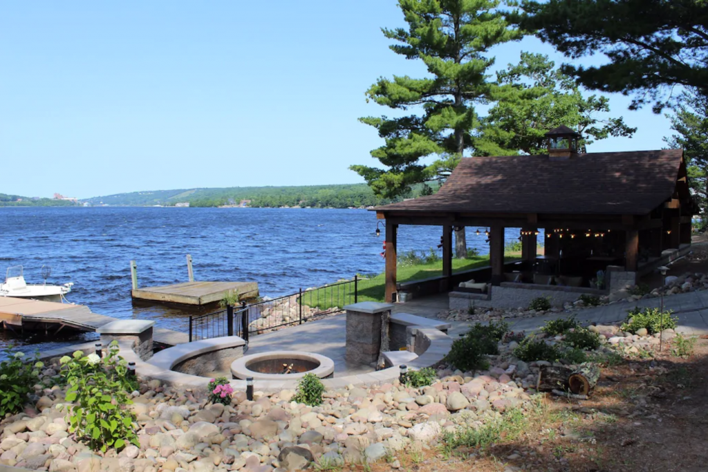 A small gazebo with a fire pit on the shore of a lake - Kemp's Portage Lake Log Home with Firepit and Pavilion in Houghton.