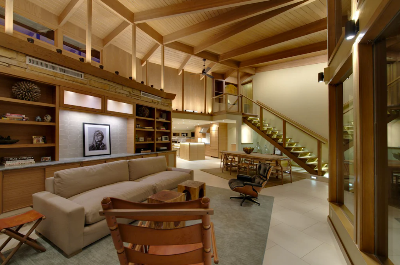 A large living room with tall, vaulted ceilings made with wood beams, built-in bookshelves lining the walls, and a cozy seating area with a large couch and accent chairs.