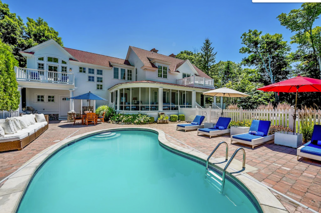 A pool with lounge chairs and umbrellas in front of a house -Lakefront Retreat with Private Beach in South Haven.