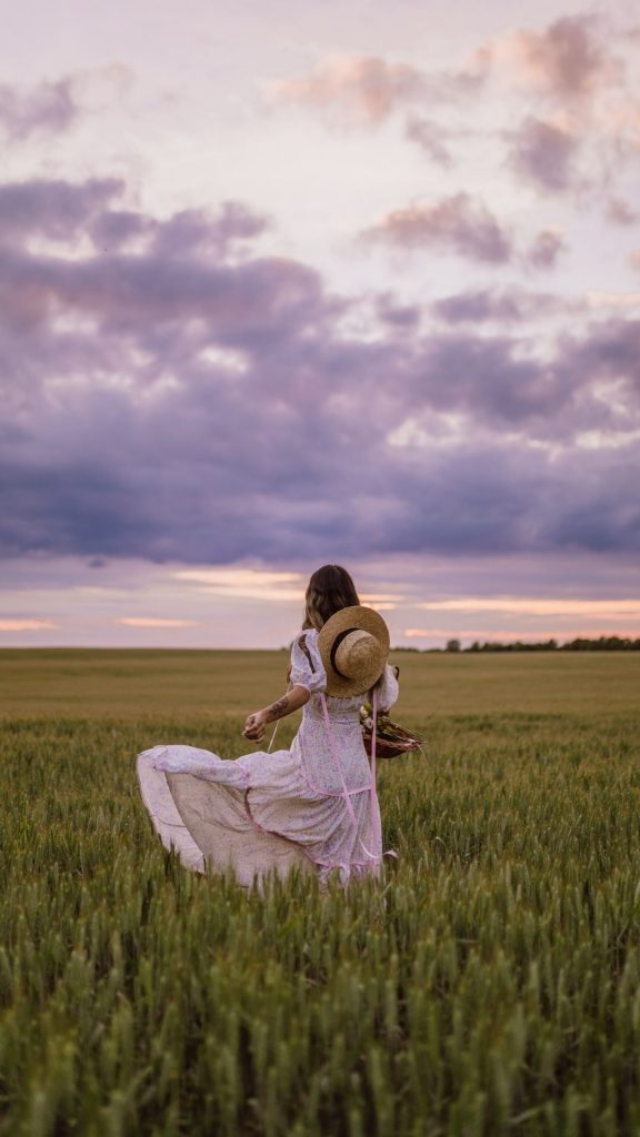 Photo of woman in a flowy cottagecore dress posing at the center of a field