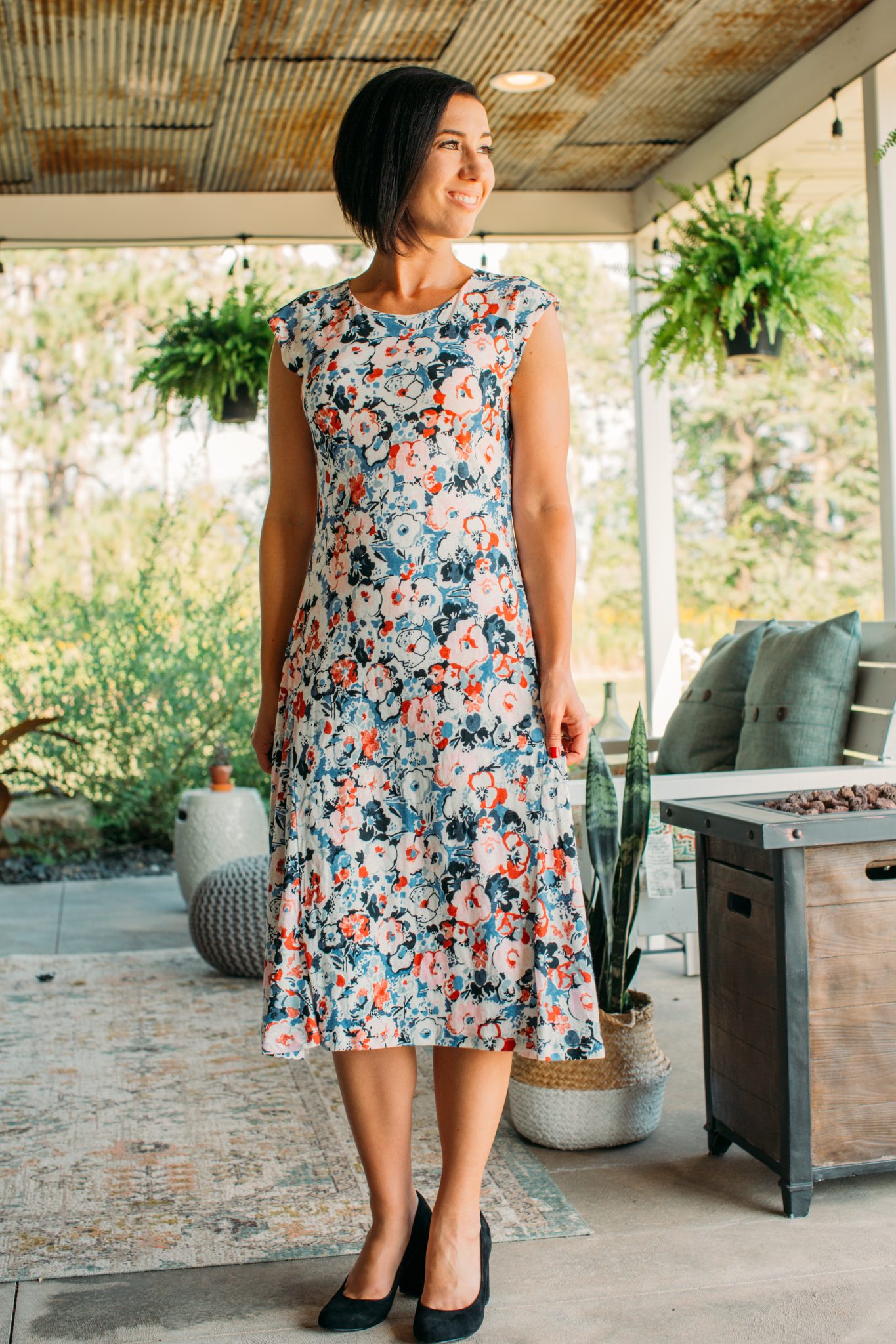 A woman wears a colorful floral printed Ralph Lauren midi dress. The dress has colorful orange and blue flowers throughout, with short cap sleeves and a high neckline. 