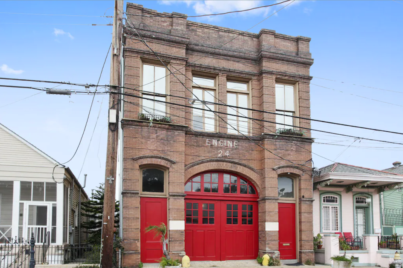 The exterior of an old firehouse in New Orleans' French Quarter. The brick façade has Engine 24 signage and red firehouse doors.