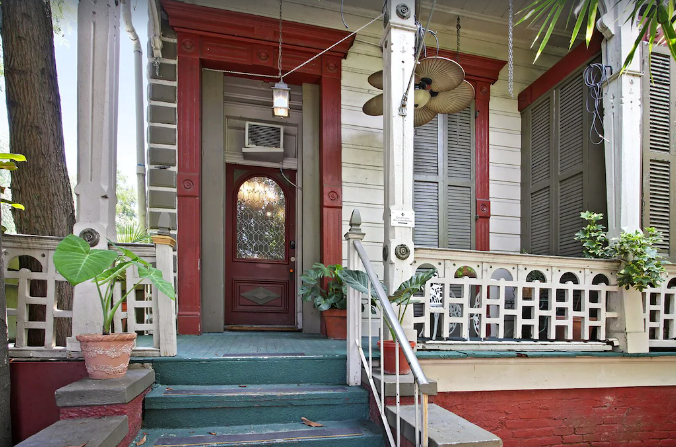The front porch of an old "haunted" New Orleans home. The porch is painted teal green with white siding and bannisters and red trim around the windows.