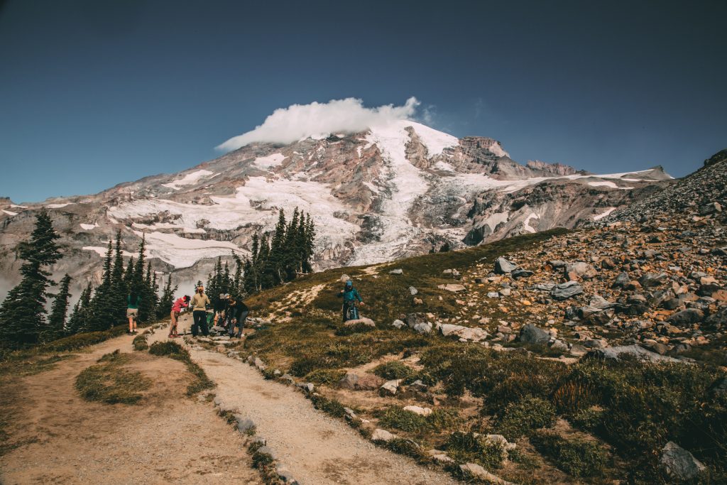 Mount Rainier with snow on the side and a hiking trail with hikers in the foreground