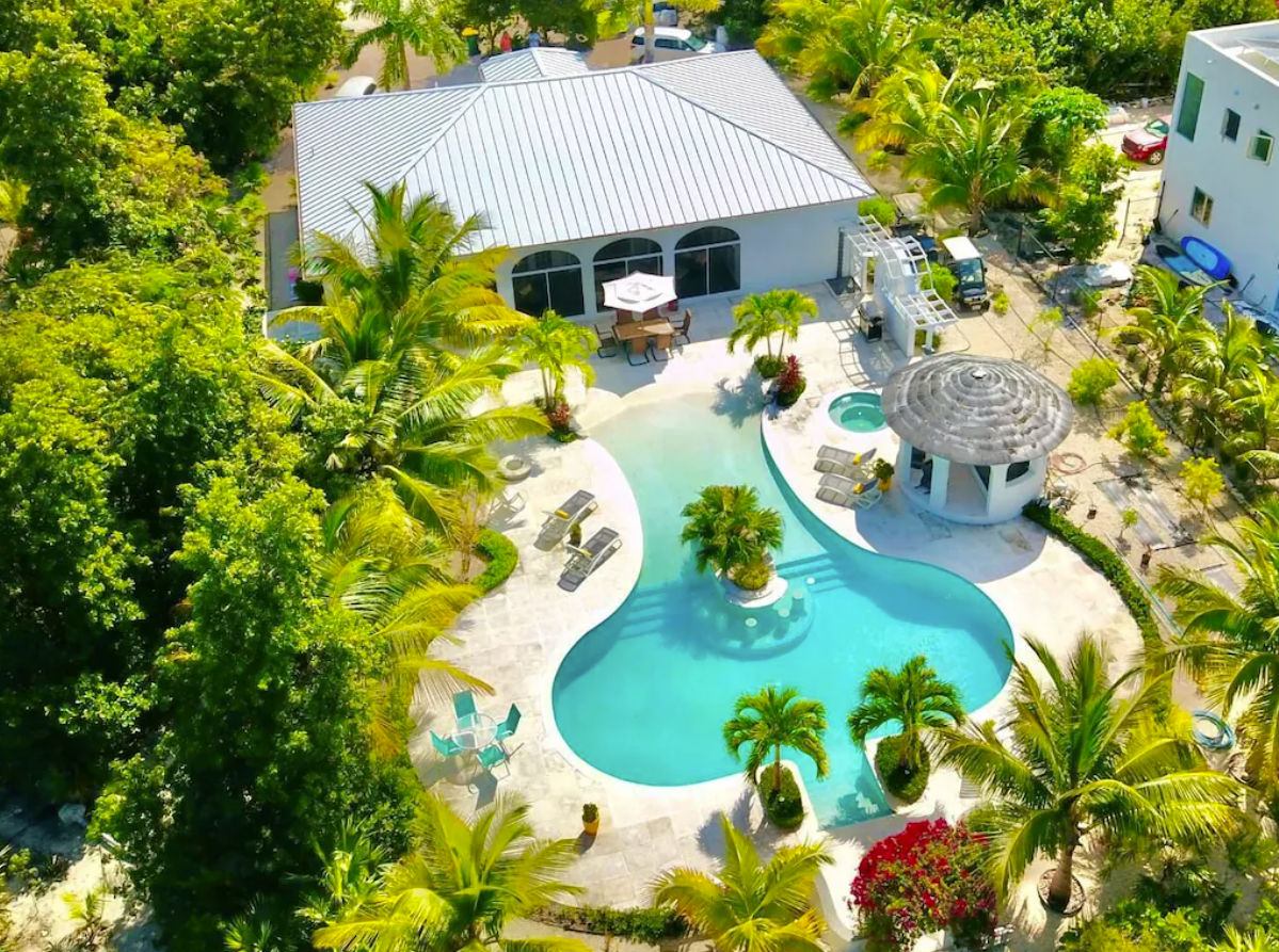 An aerial view of a private Turks and Caicos rental home shows a ranch-style villa with a private pool area, jacuzzi, and cabanas surrounded by privacy landscaping.