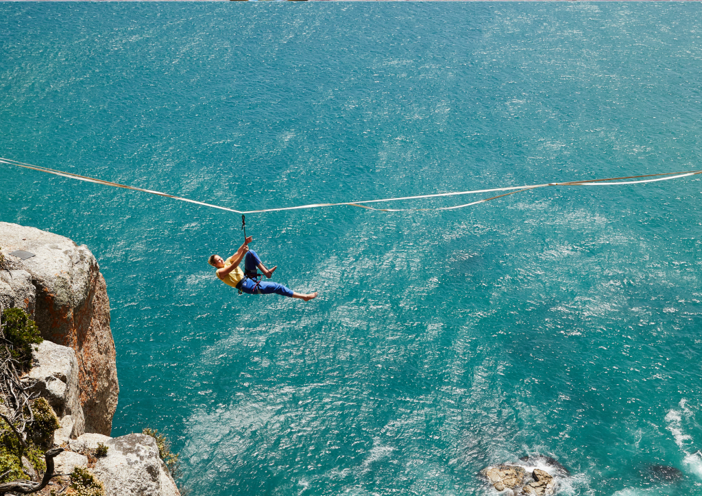 A person on a zip line on a cliff overlooking the ocean.