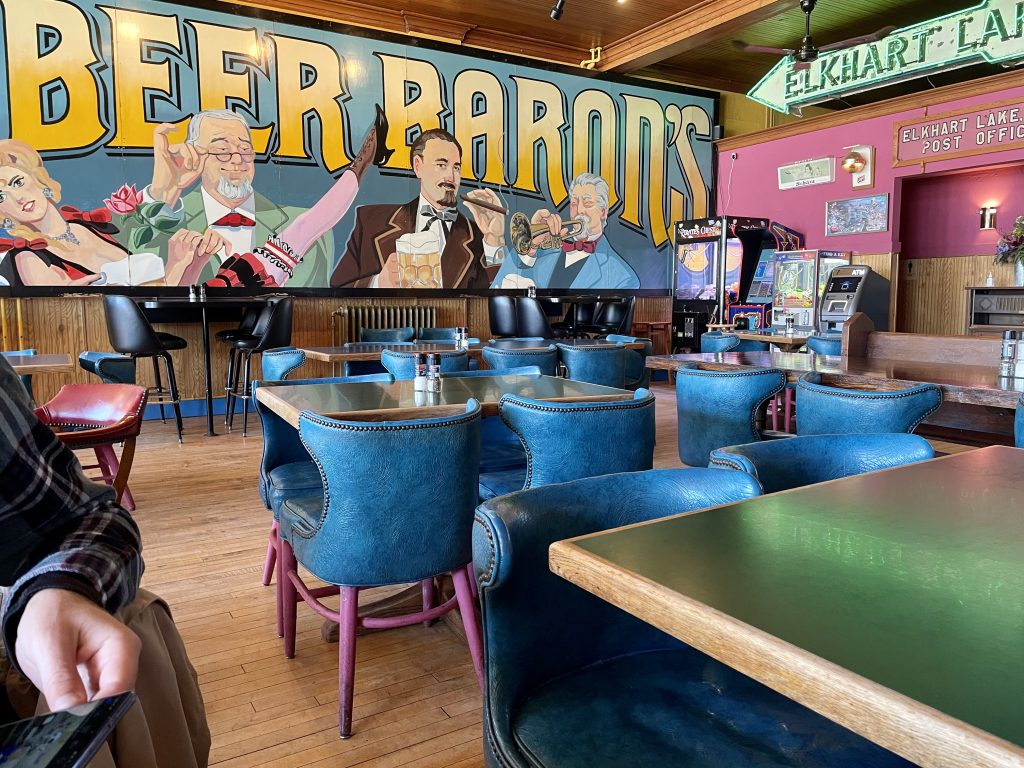 The inside of Lake Street Cafe boasts a large wall mural of Beer Barons, comfortable dine-in seating, and some arcade games.