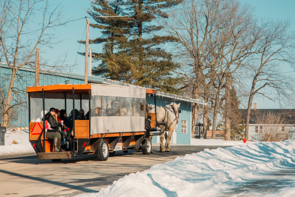 Visitors take a horse-drawn carriage ride down snowy streets on a clear sunny day in Elkhart Lake, Wisconsin