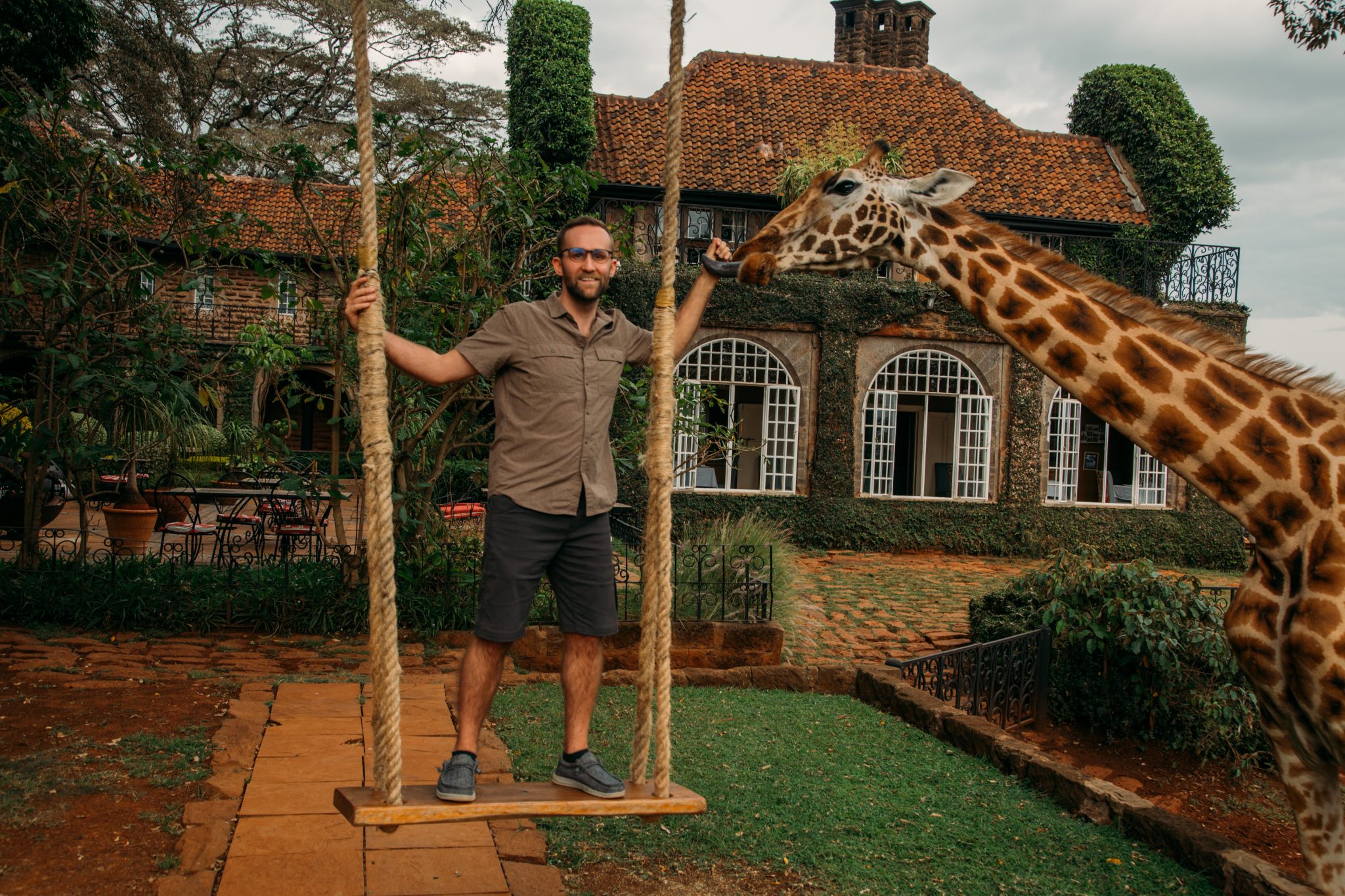 A man standing on a swing next to a giraffe.