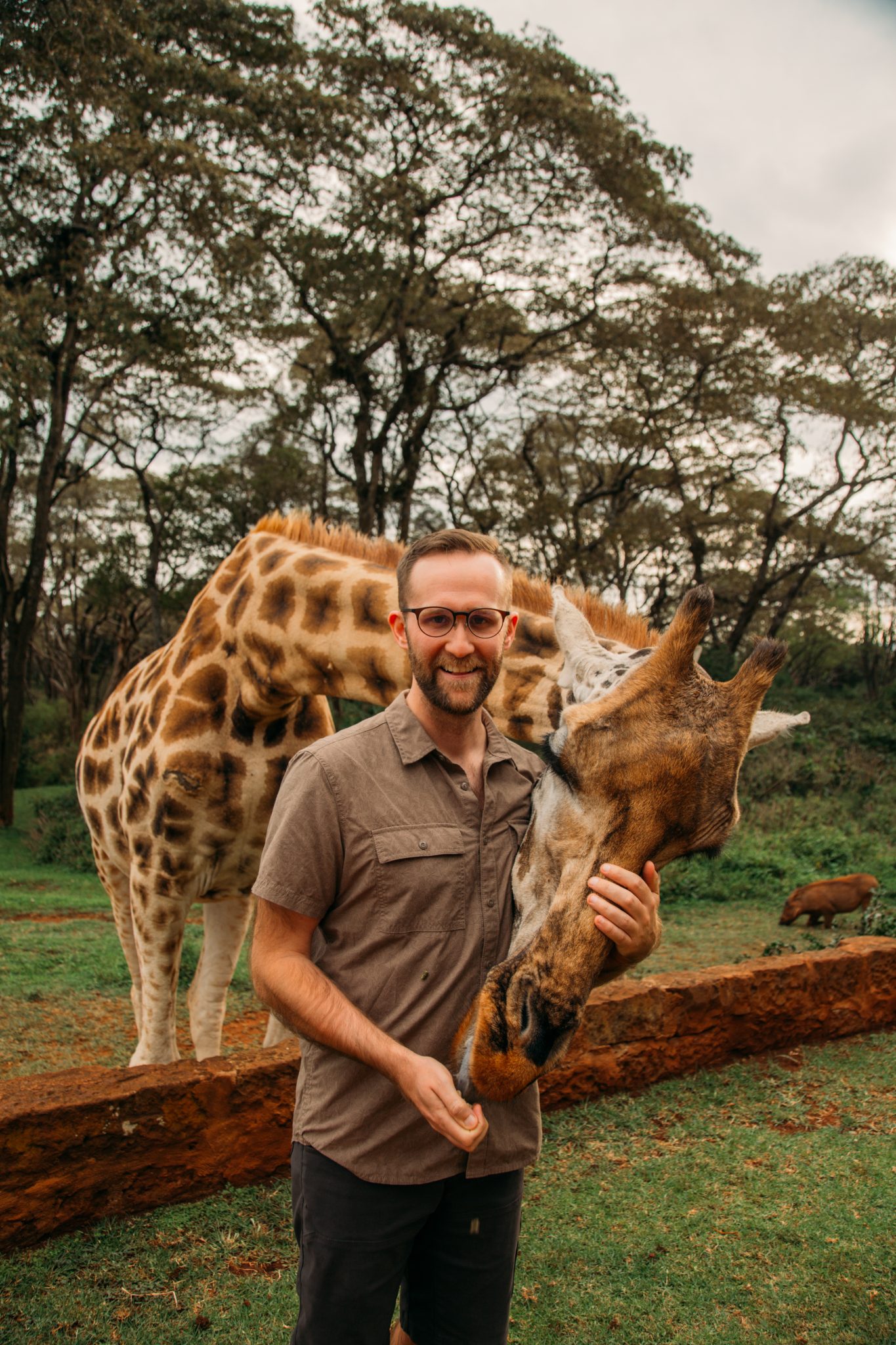 A man is petting a giraffe and smiling at the camera.