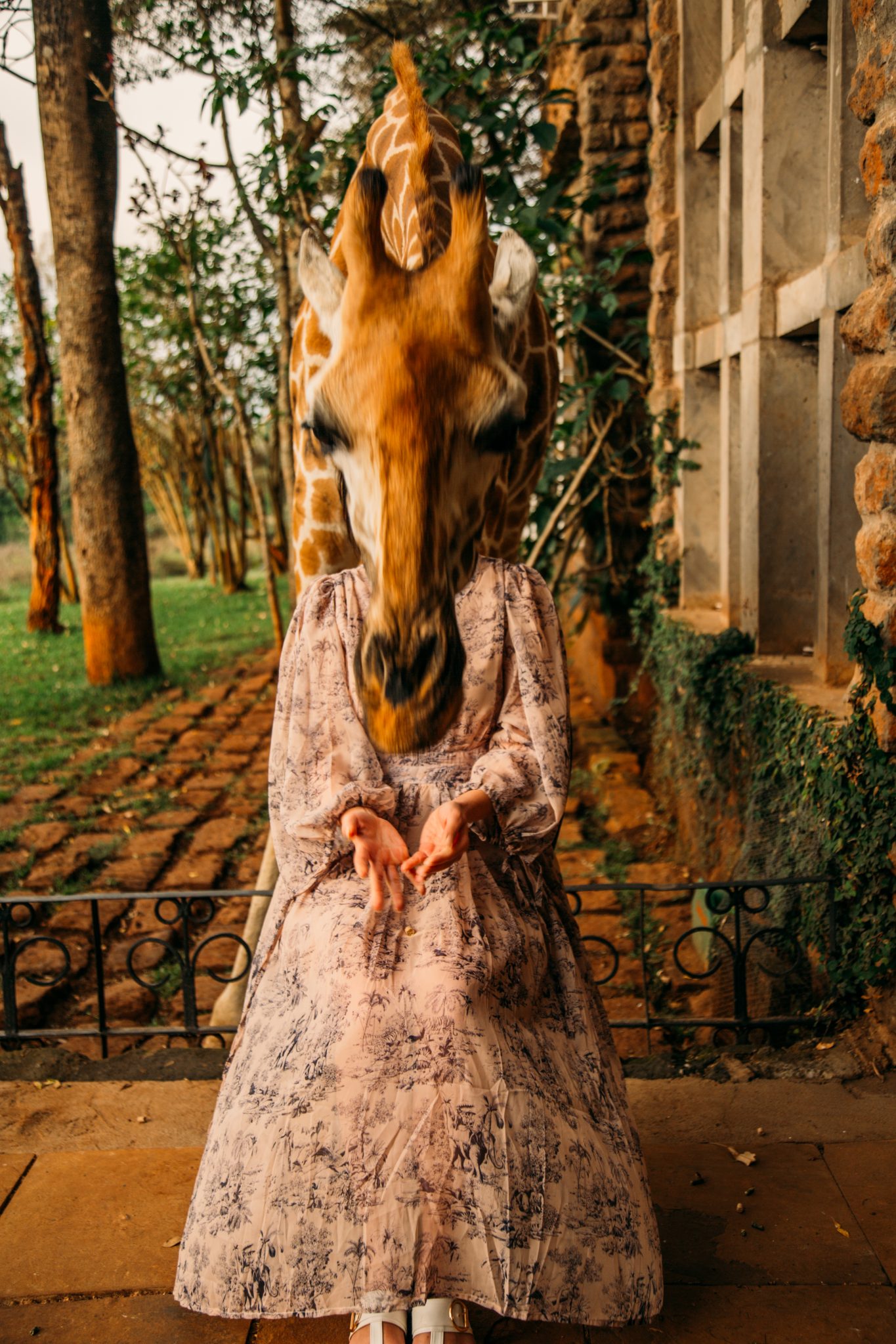 A woman wearing a dress and a giraffe on top of her to create an optimal illusion. 