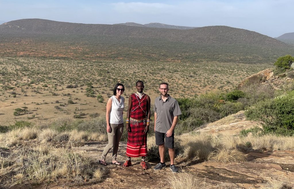 A man and woman standing next to their African guide during a safari. 