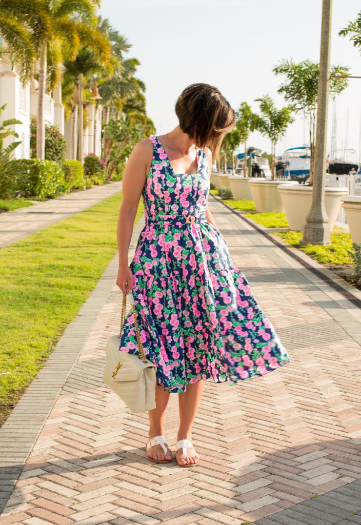 Lindsey of Have Clothes, Will Travel wearing a pink and navy floral midi dress with palm trees lining the sidewalk behind her