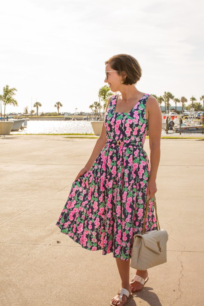 Lindsey wearing a pink floral McKinnon Midi Dress by Lilly Pulitzer holding a YSL Loulou bag in a tropical location